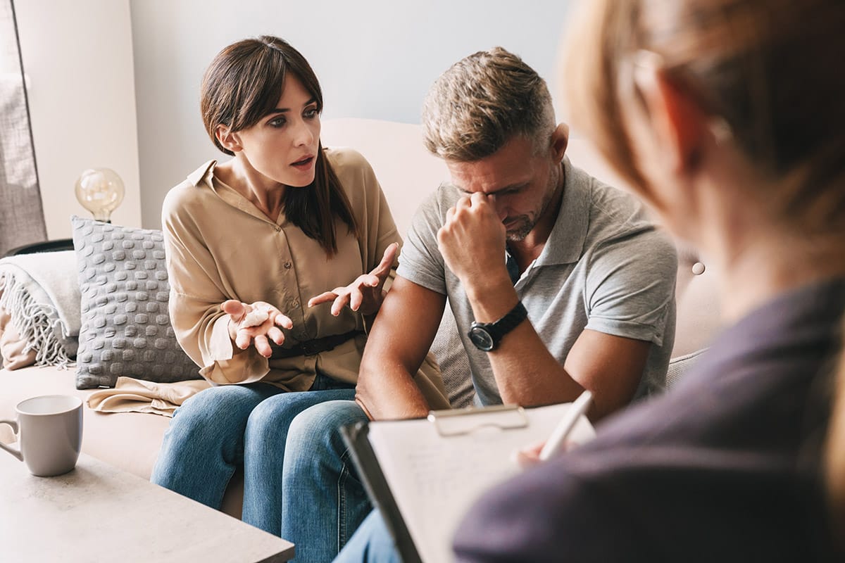 two people fight and cry on a couch with a therapist after seeking family therapy