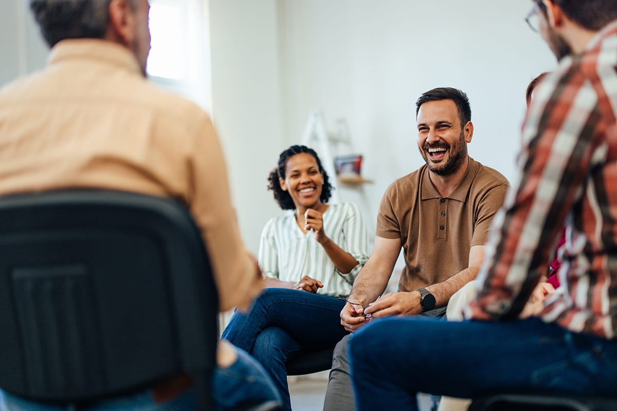 a group of people sitting in chairs laughs as they participate in group therapy in Massachusetts