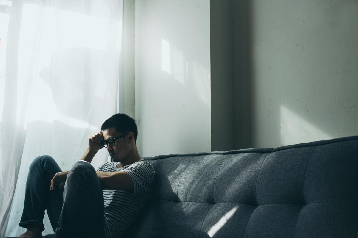 a person sits on a couch in a dark room lit only by sunlight as they experience substance abuse and trauma