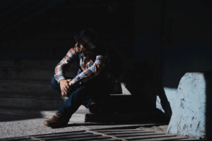 a person sits on a stoop in the dark while struggling with alcohol dependence