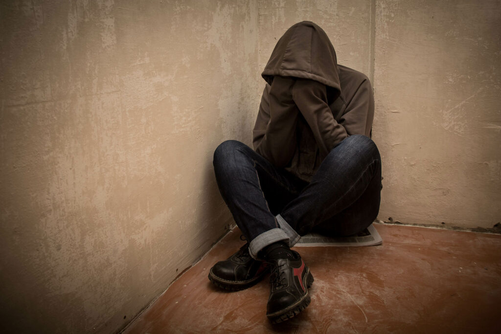 a person wearing a hoodie sits in the corner of a room struggling with cocaine withdrawal symptoms