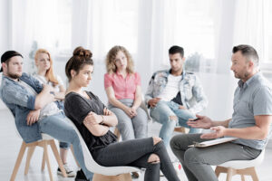 a group of people sit facing one other person in a drug rehab program