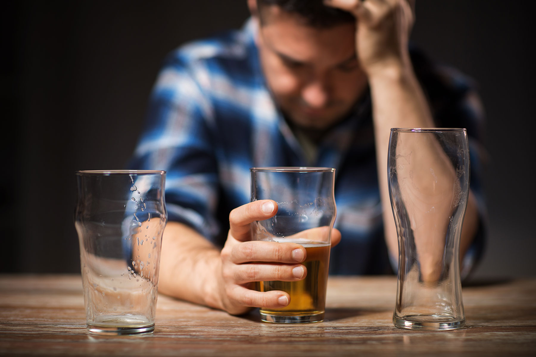 a person with two empty beer glasses in front of them holds a half-full beer glass and looks pained to show alcohol and the brain