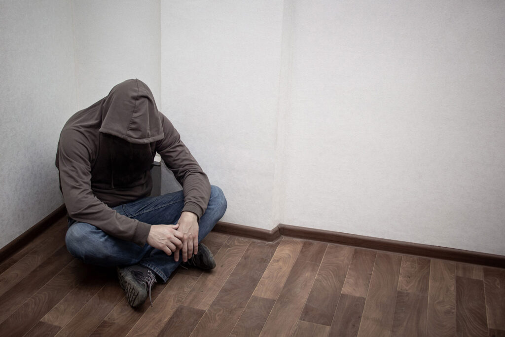 a person sits in a corner of a room in a hoodie to show side effects of meth abuse