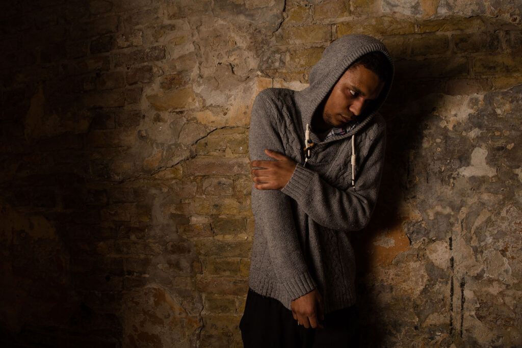 a person leans on a stone wall in a hoodie as they show symptoms of crack abuse