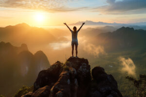 a person at the peak of a mountain with their arms raised to show the benefits of detox