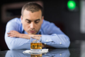 a person looks sad in front of a glass of whiskey to show alcohol and depression