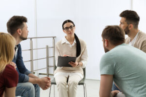 a group of people sit in chairs and talk during group counseling