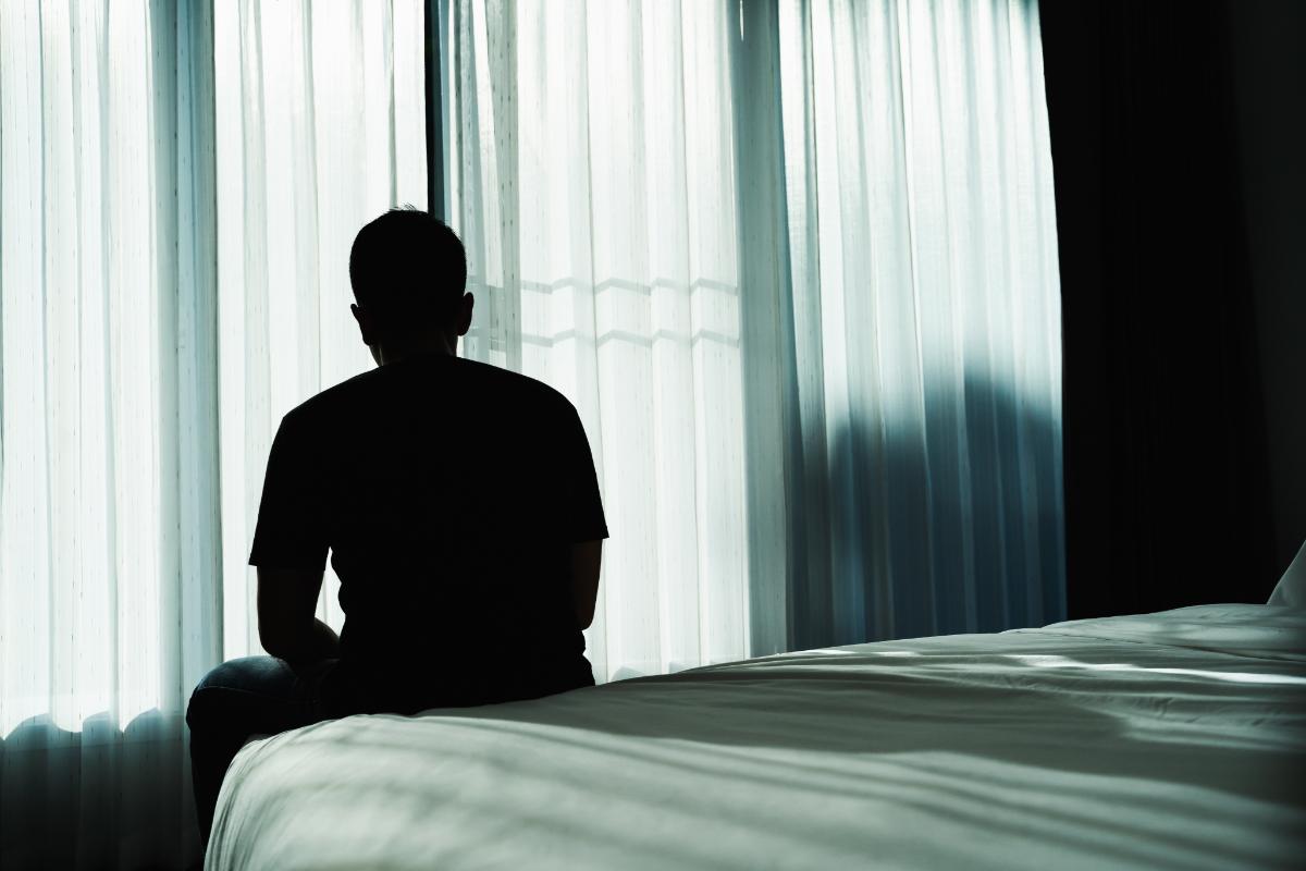 a person sits on a bed in the dark to show heroin side effects